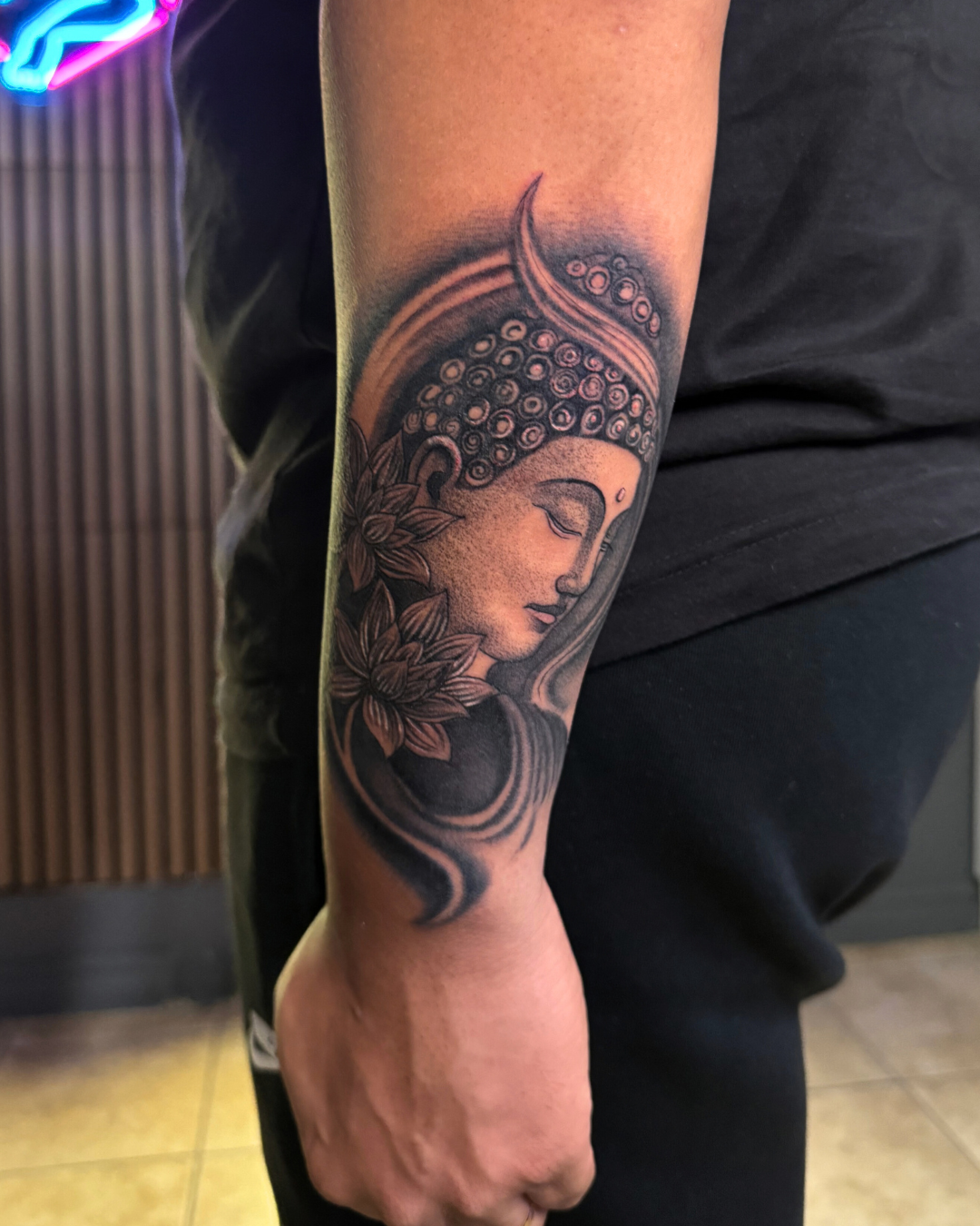 Black and grey portrait of Buddha with lotus flowers on the forearm