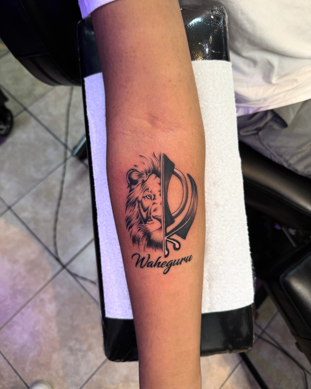 Black and grey split face of a lion and Khanda symbol with Waheguru script on the forearm