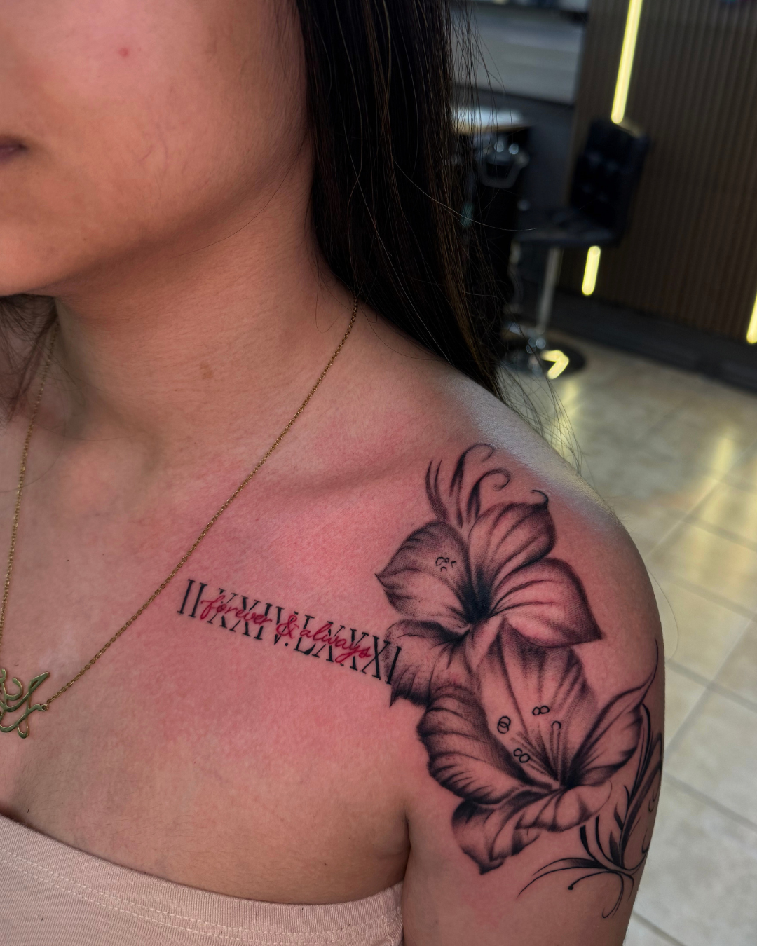 Black and grey floral tattoo with red Roman numerals on the collarbone