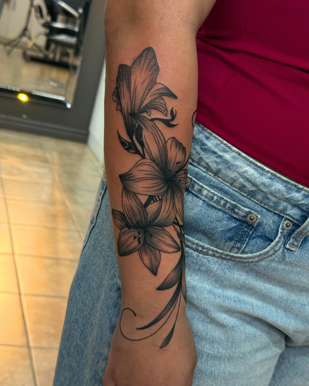 Black and grey floral lilies wrapping around the forearm