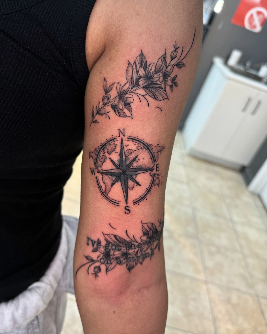 Fine line compass and world map with floral vines and script reading I've got the world on a string