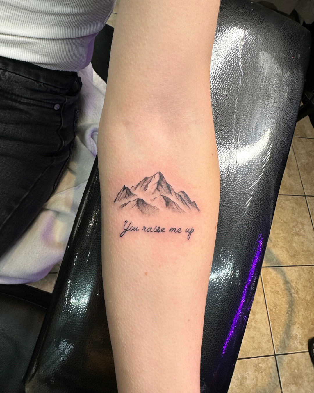 Fine line mountain range tattoo with script You raise me up on the forearm