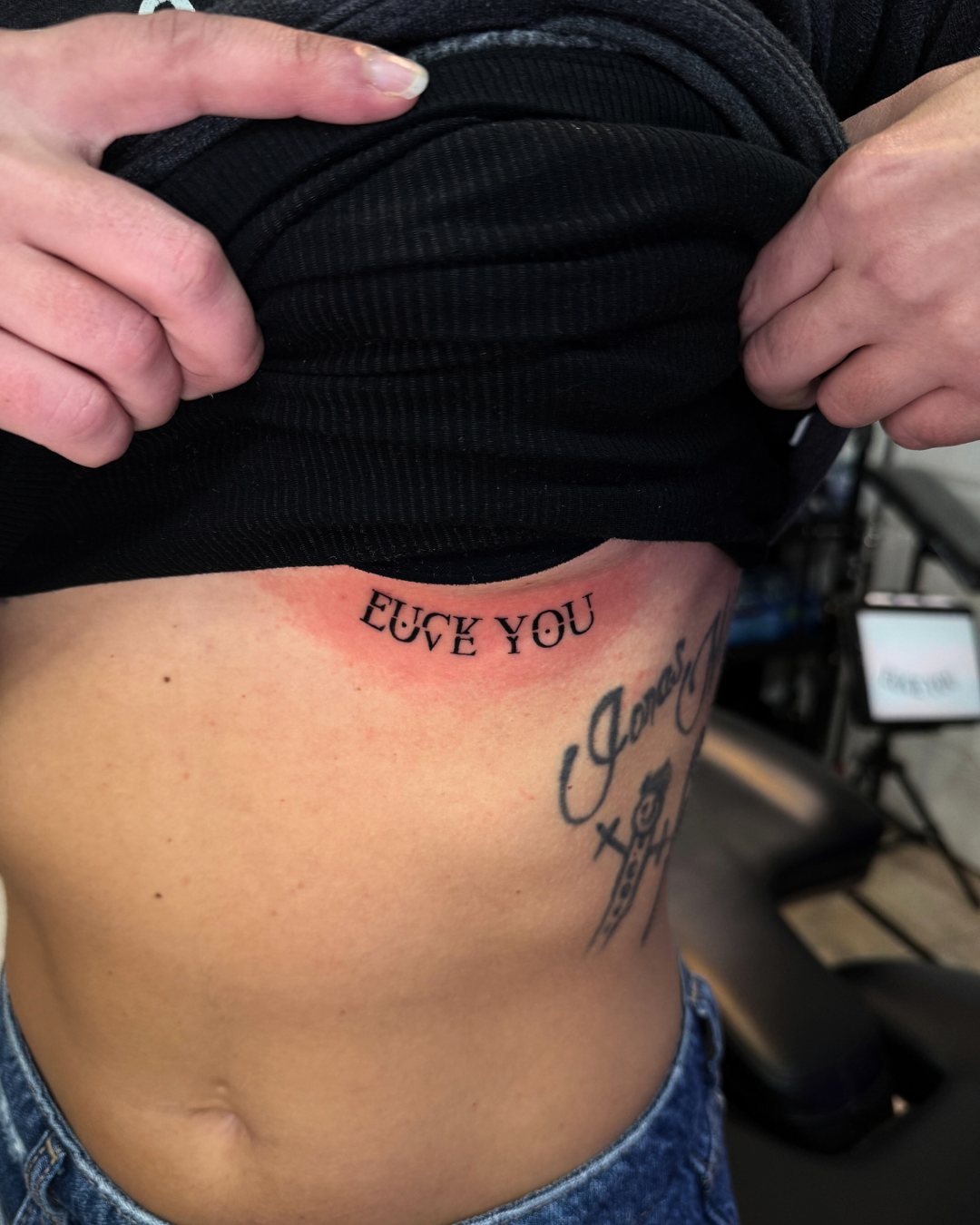 Fine line script tattoo reading FUCK YOU on the ribcage area