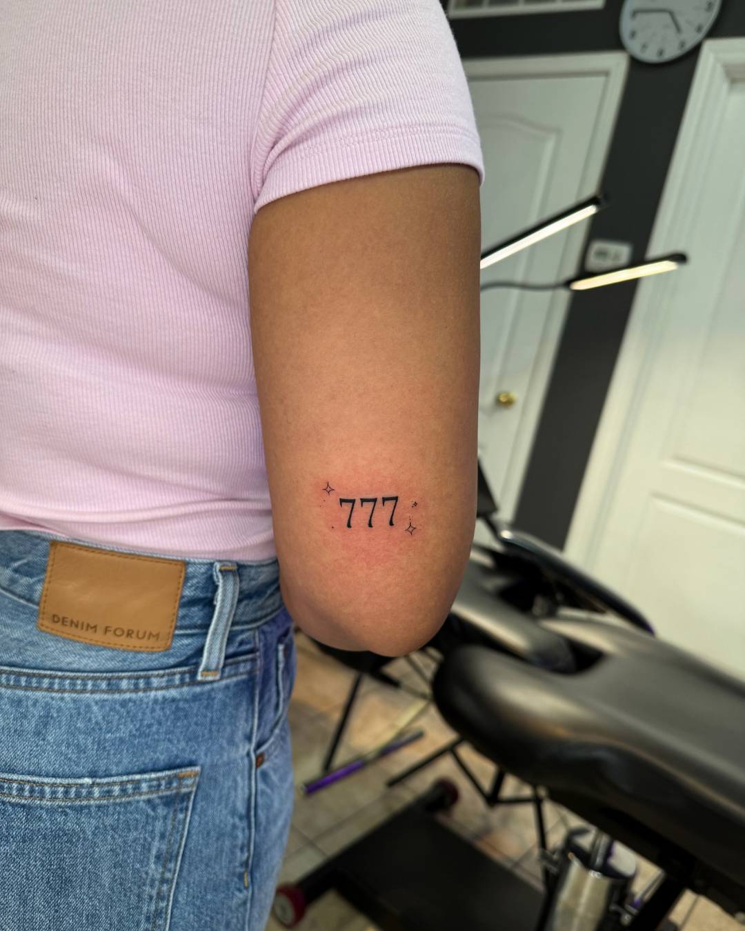 Small fine line numbers 777 with sparkle details above the elbow