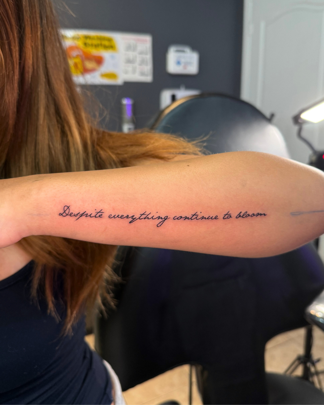Fine line cursive script reading Despite everything continue to bloom on the forearm