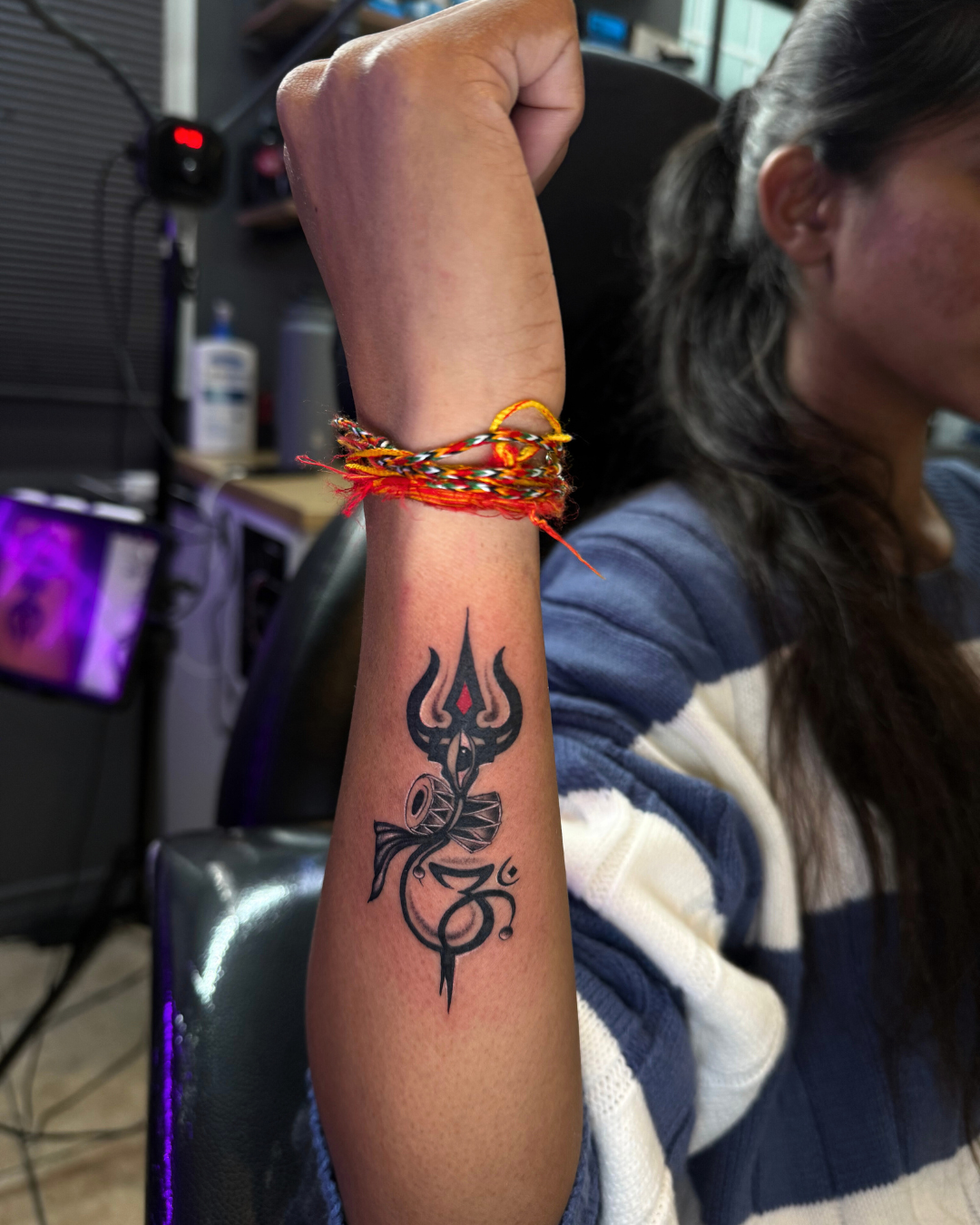 Fine line tattoo of a trishul, damaru, and Om symbol on the forearm