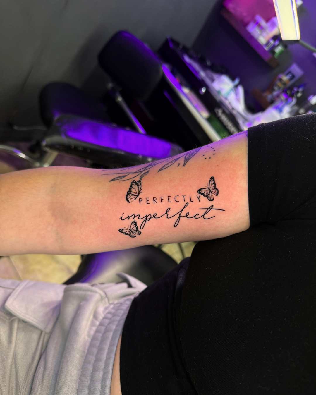 Script tattoo reading PERFECTLY imperfect surrounded by three small butterflies on the arm