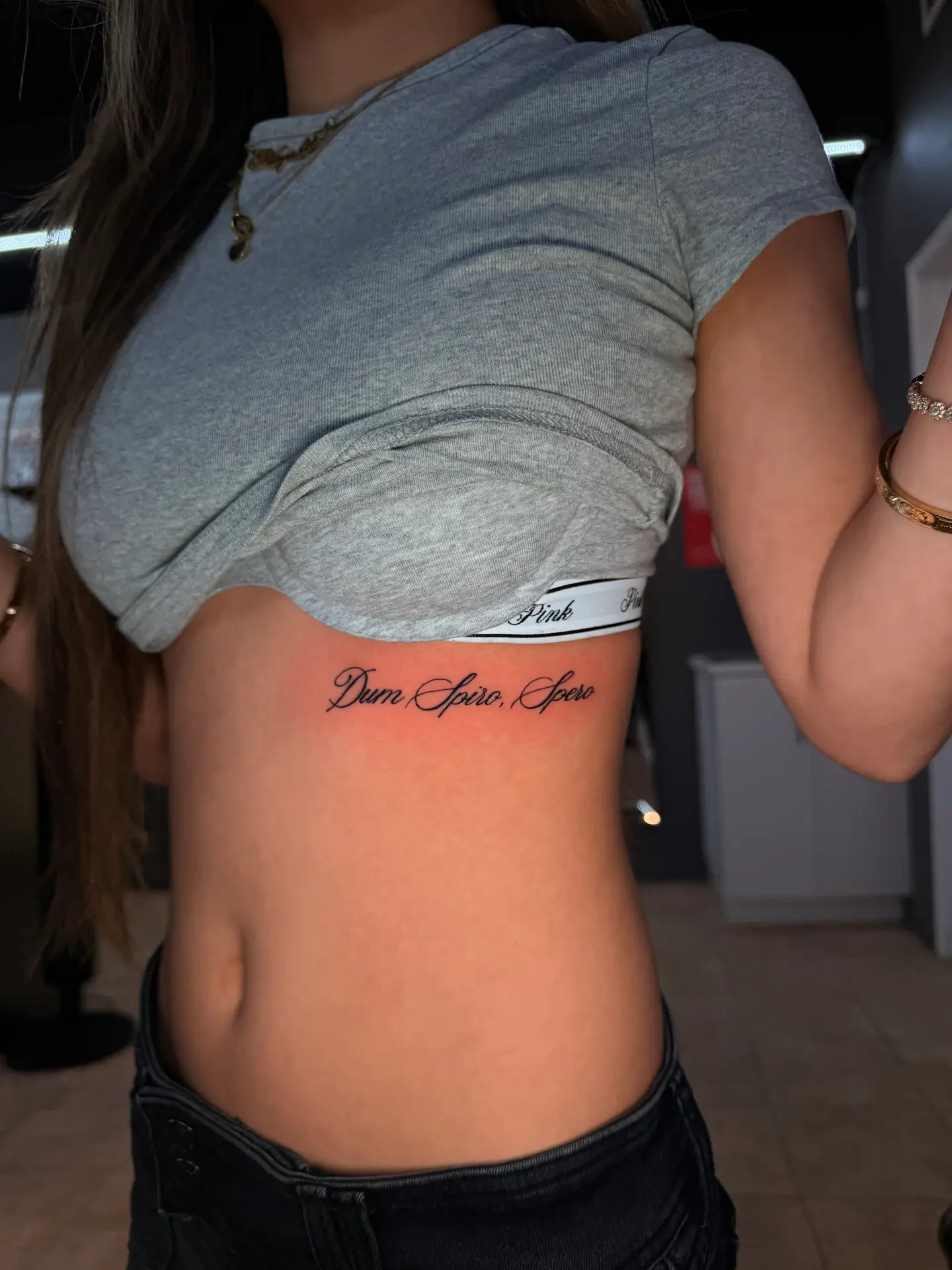 Fine line cursive script tattoo along ribcage in Latin calligraphy