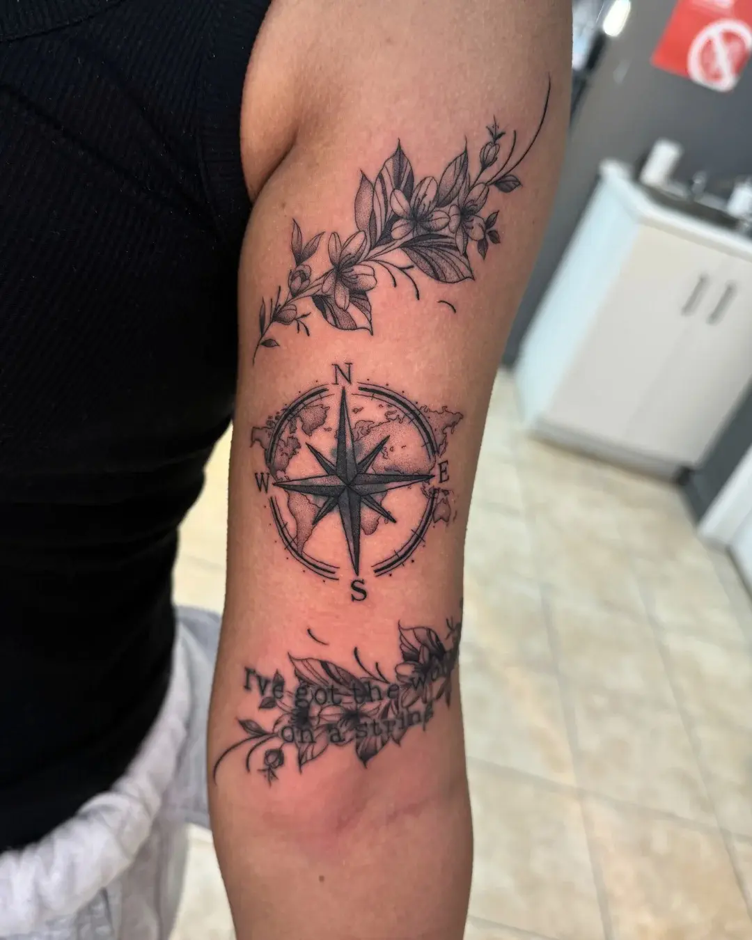 Fine line compass and world map with floral vines and script reading I've got the world on a string