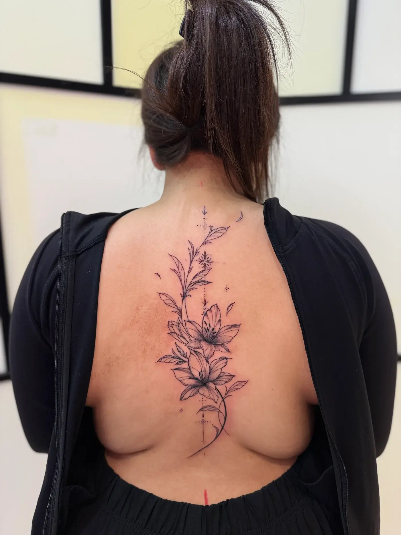 Fine line lily flower tattoo cascading down spine