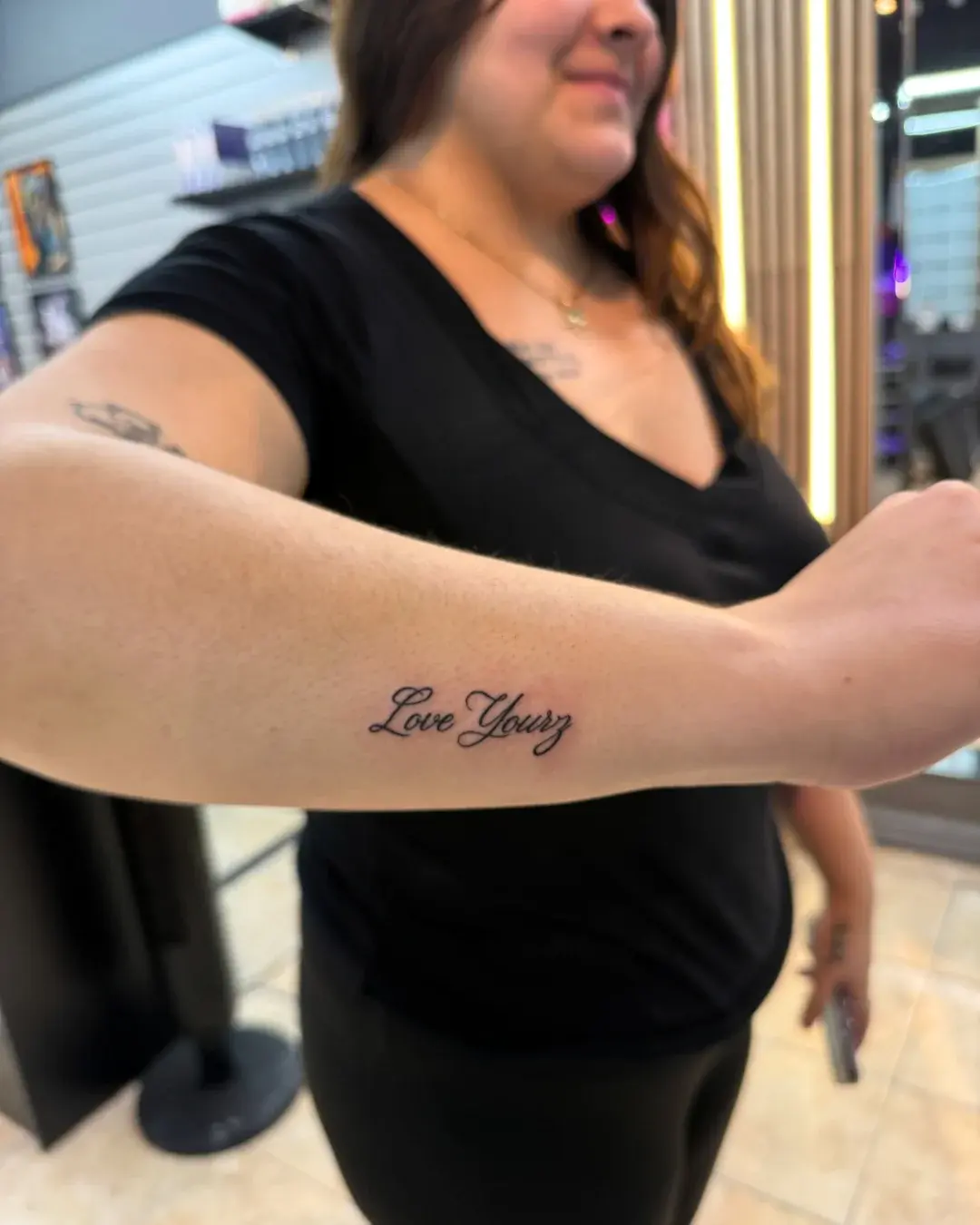 Fine line cursive script tattoo reading Love Yourz on the forearm